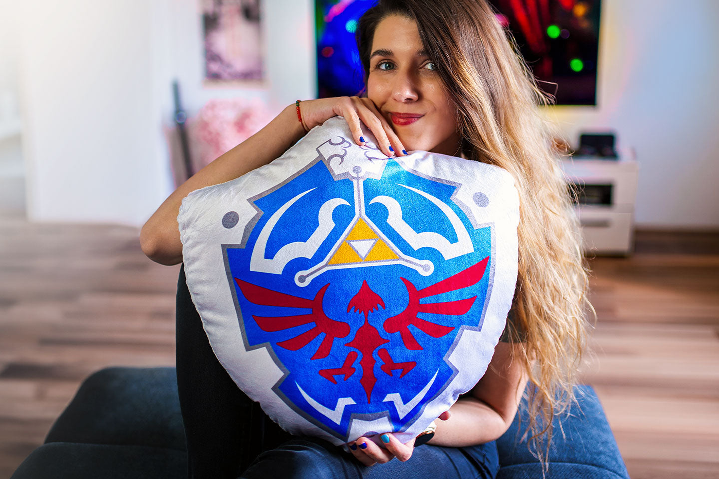 Eine Person sitzt in einem gemütlichen Wohnzimmer und hält ein großes Zelda Hylia Shield Kissen in den Armen.